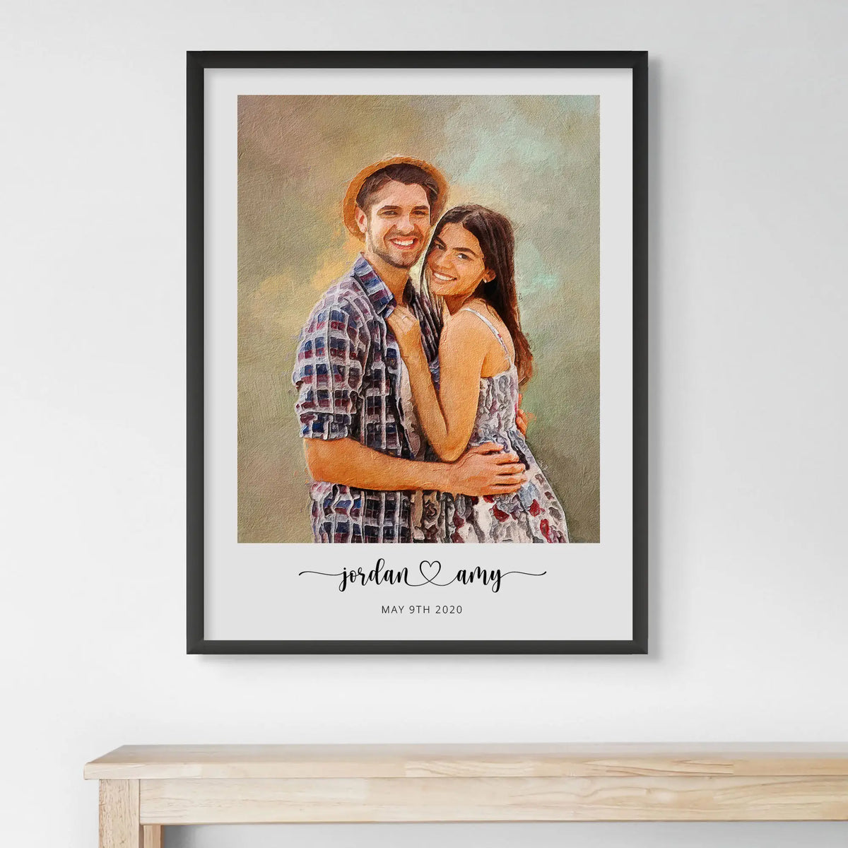 Oil-style portrait of a smiling couple, the man in a straw hat, in a black frame above a light wood table