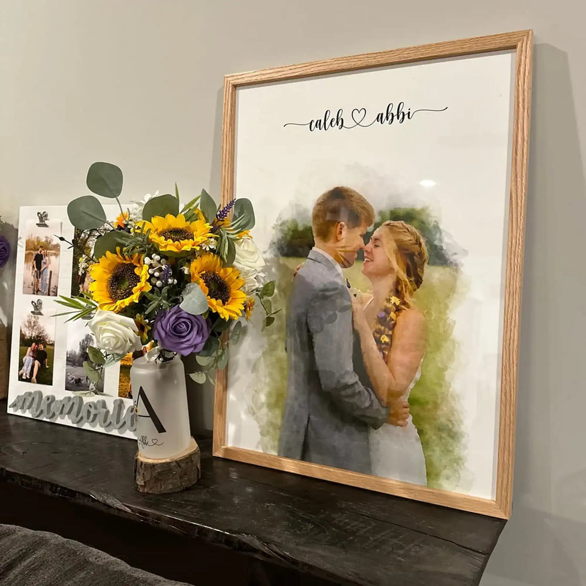 Customer photo of a watercolor-style portrait of a couple in a light oak frame, on a dark shelf beside sunflowers