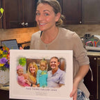 A smiling woman holds a white-framed watercolor-style family portrait of four titled 'This Thing Called Love'
