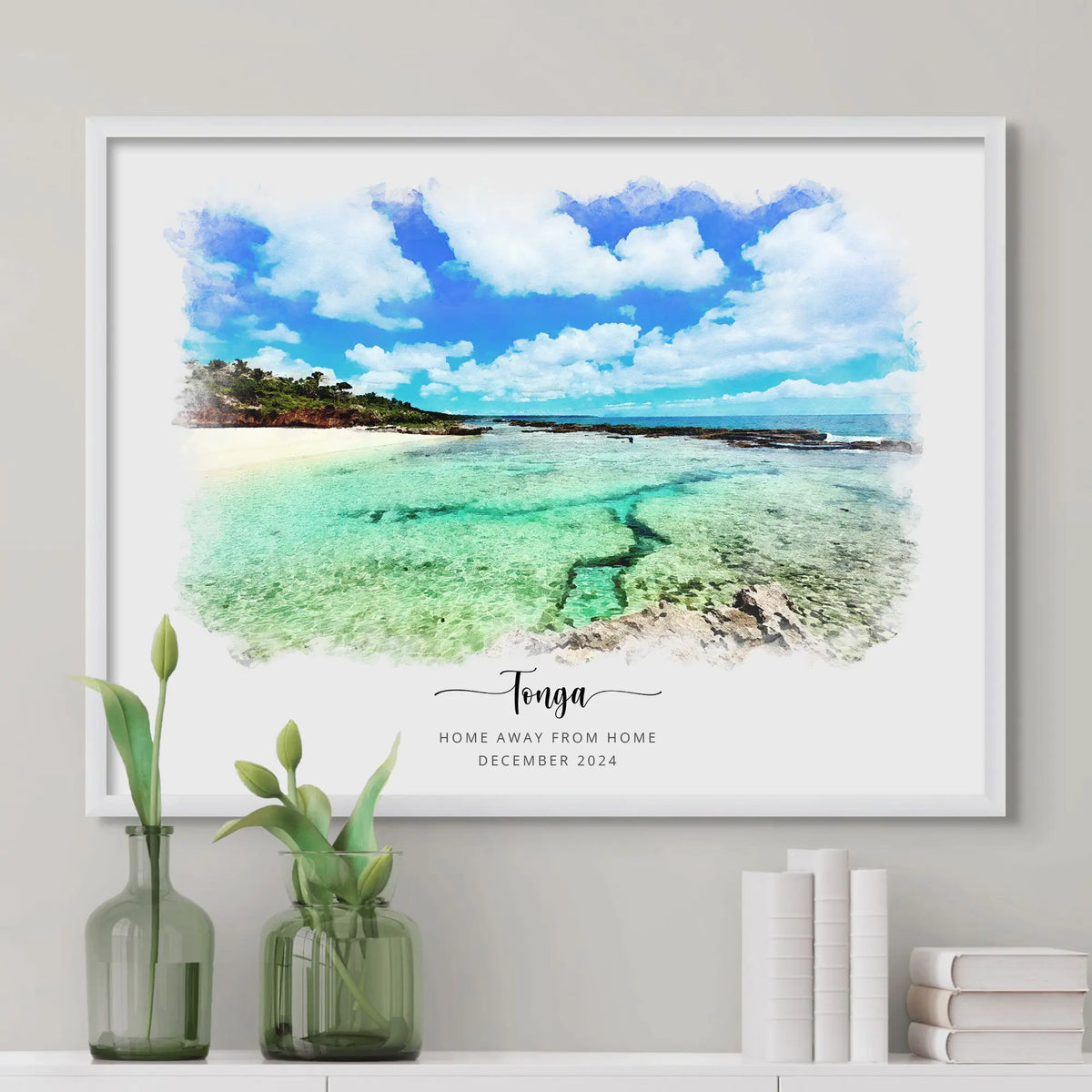 Watercolor-style portrait of a turquoise tropical shoreline, framed in white above a shelf with books and green vases