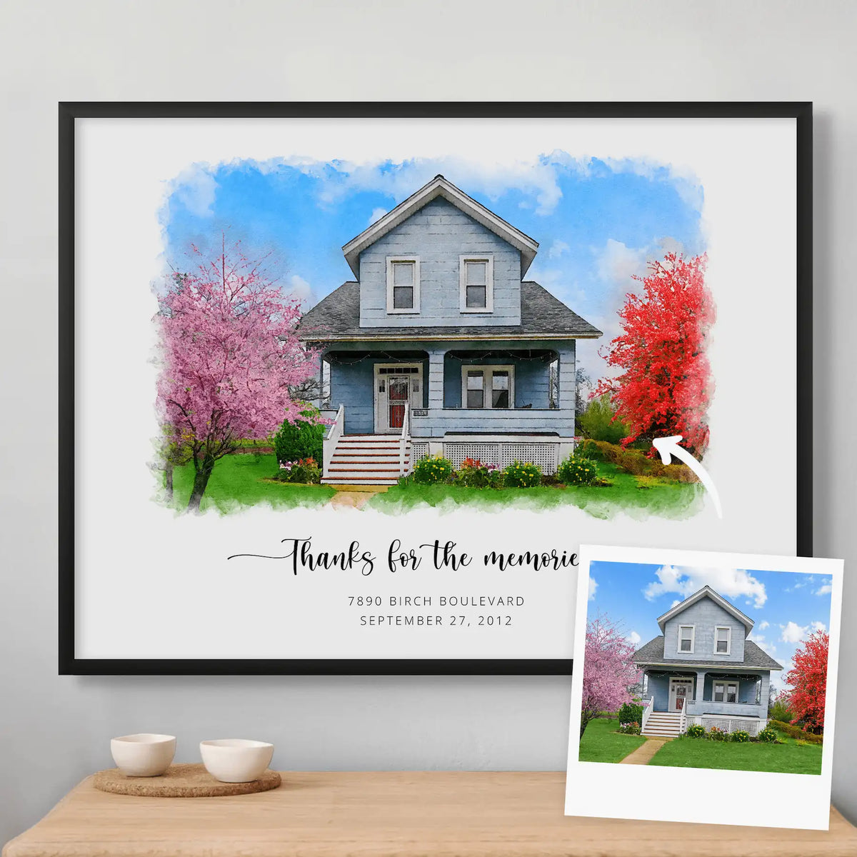 Watercolor-style portrait of a blue two-story house between blossom trees, framed in matte black, beside its photo