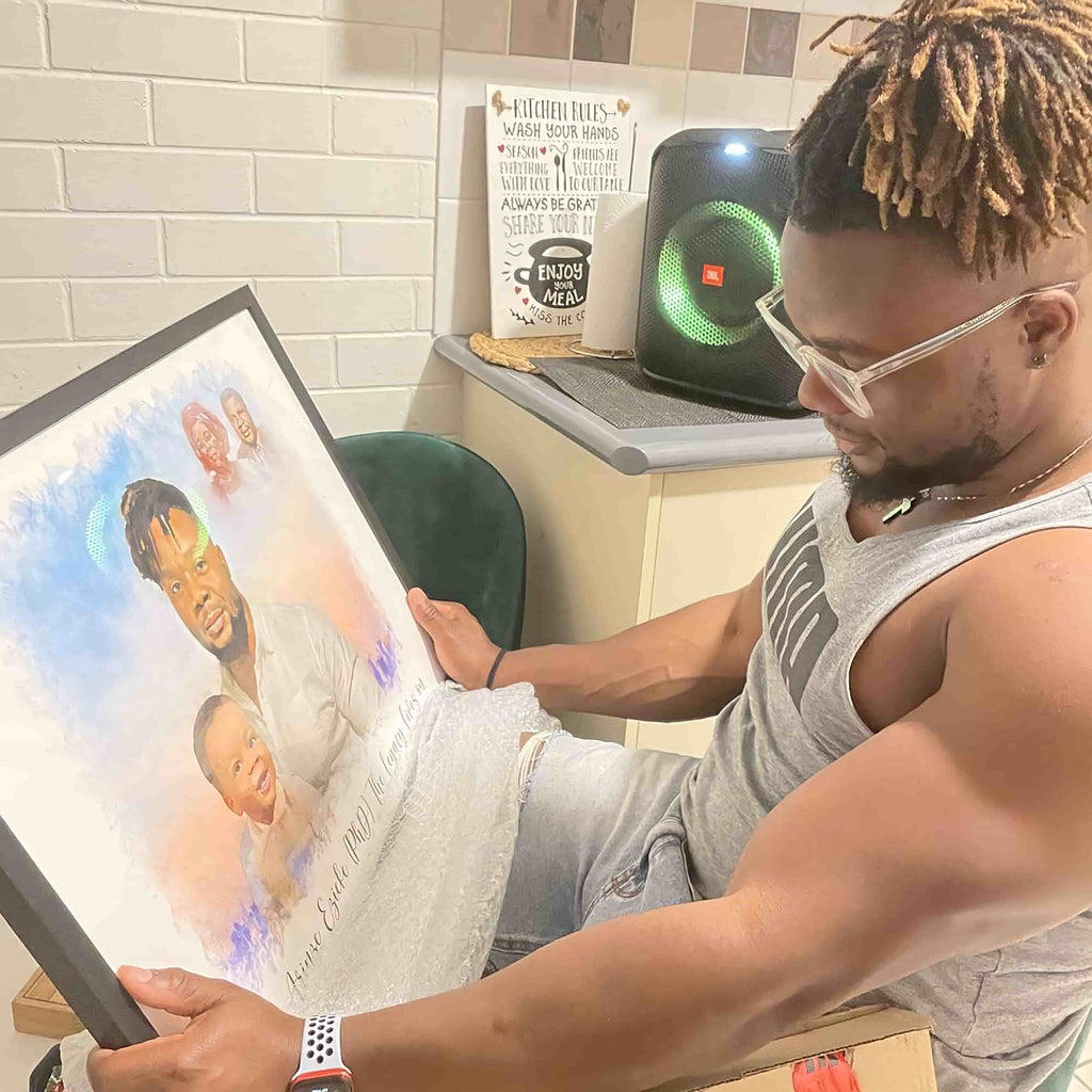 A man looks down at a black-framed watercolor-style portrait of a man and a child, partly unwrapped from bubble wrap